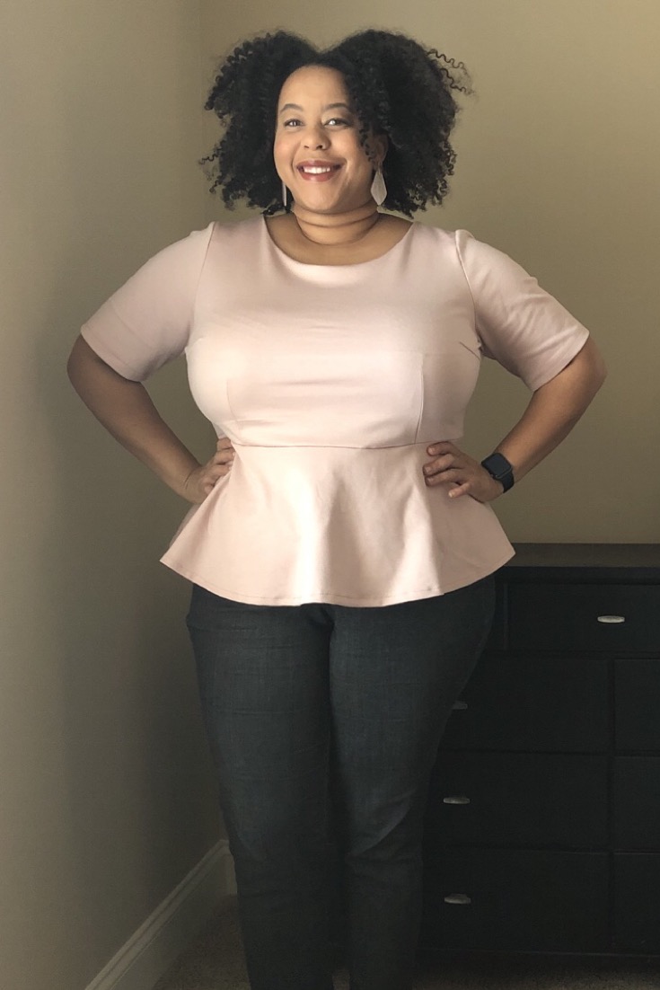 Sierra is facing the camera  with her hands on her hips wearing a pale pink peplum top.